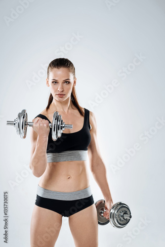 Strong girl holding dumbbells on a grey background