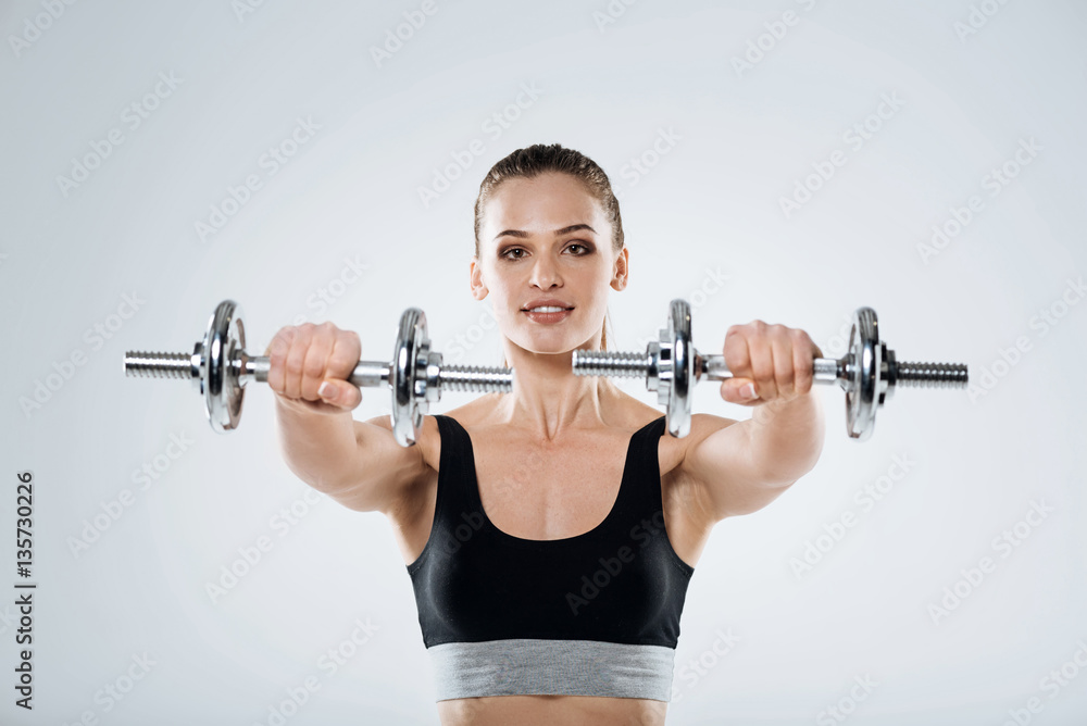 Happy girl exercising with dumbbells on a grey background Happy girl exercising with dumbbells on a grey background