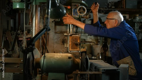 Tracking sequence of man drilling through metal with an old fashioned drilling machine in his workshop.