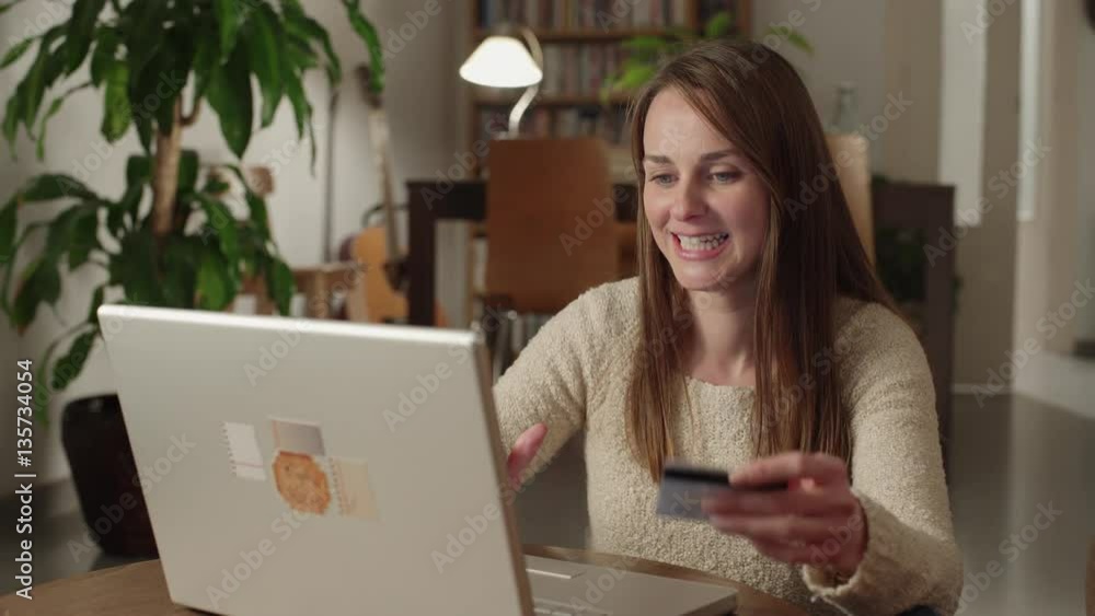 Young woman shopping using her credit card and laptop at home. She is in her living room at night. Young woman shopping using her credit card and laptop at home. She is in her living room at night.