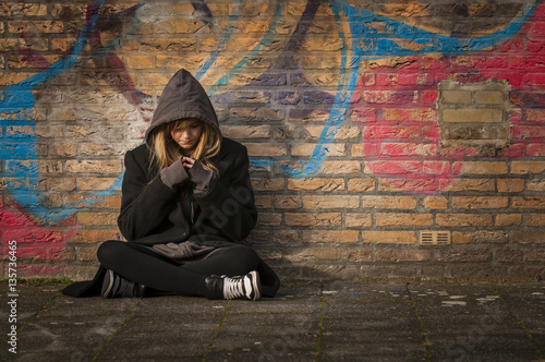 runaway girl sits in front of a wall with graffiti