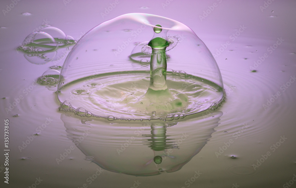 ein grüner Wassertropfen beim Eintritt in eine Seifenblase