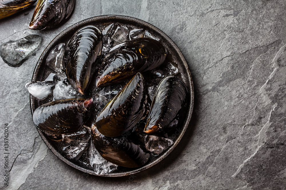 Fresh uncooked big mussels on ice. Slate background. Top view Fresh uncooked big mussels on ice. Slate background. Top view