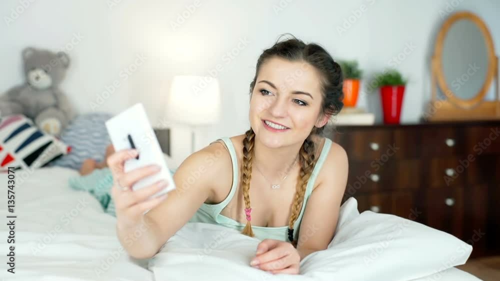 Happy girl wearing pyjamas and lying in bed while doing selfies on smartphone, steadycam shot
Happy girl wearing pyjamas and lying in bed while doing selfies on smartphone, steadycam shot