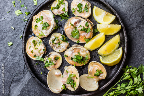 Raw clams with lemon, herbs on black iron plate