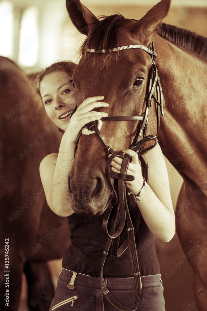 Woman hugging brown horse in stable