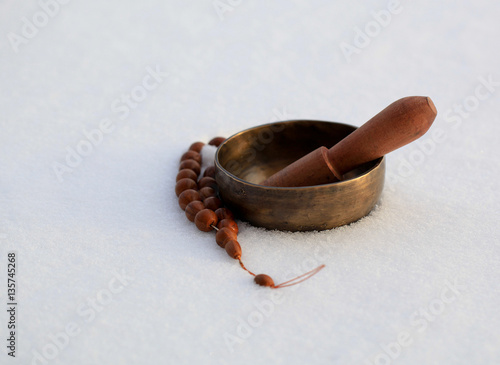 Tibetan singing bowl on a white snowy background and rosary. photo