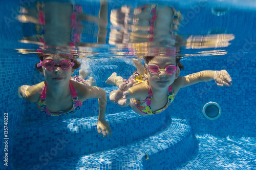 Children swim in pool under water, happy active girls in goggles have fun, kids sport on active family vacation
