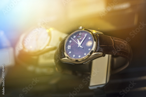 Beautiful black leather watch in front of other watches. Lens flare in background.