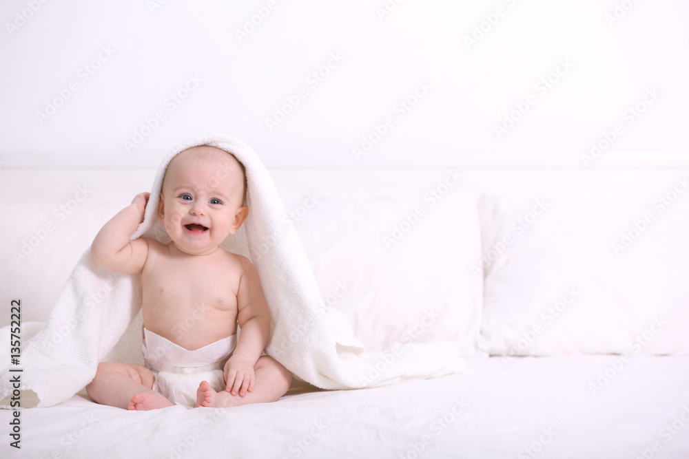 Cute funny baby with towel sitting on bed at home Cute funny baby with towel sitting on bed at home