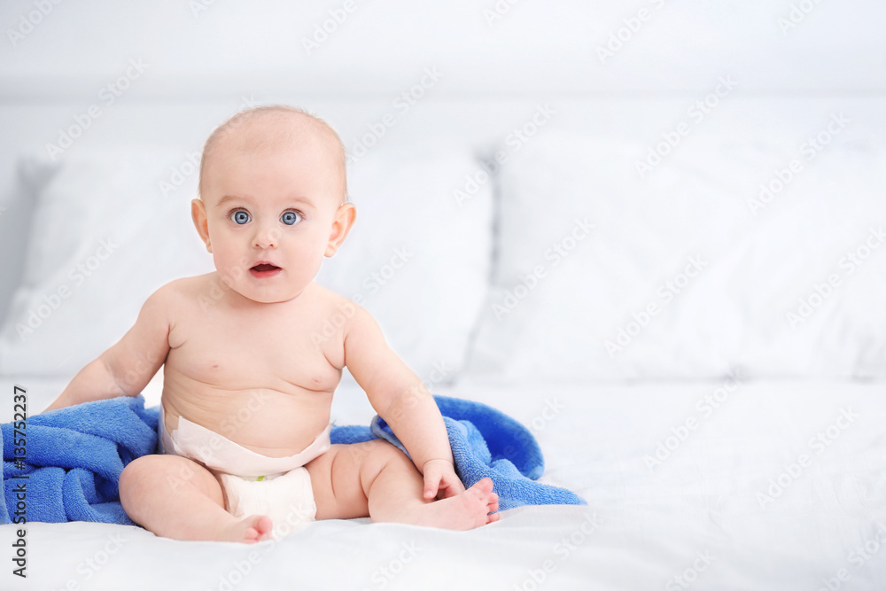 Cute funny baby with towel sitting on bed at home