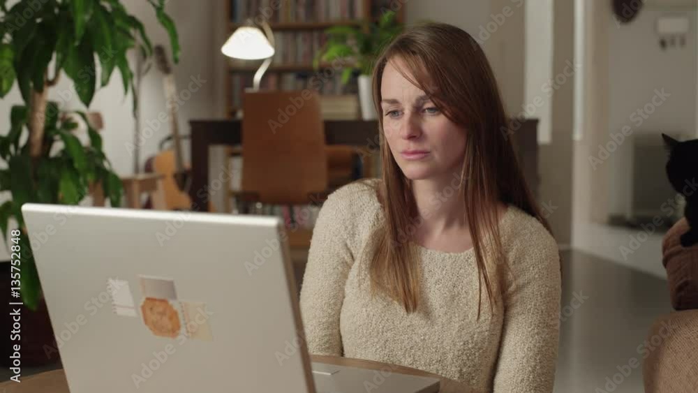 Young woman watches videos on internet in her laptop at home. She watches very concentrated and serious. Dolly shot to the left. Young woman watches videos on internet in her laptop at home. She watches very concentrated and serious. Dolly shot to the left.