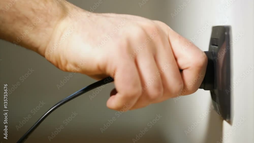 Hand detaches a plug from an electrical outlet. Hand detaches a plug from an electrical outlet.