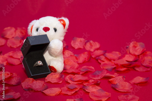 stylish luxury ring with diamond in black box and teddy bear on red background, valentine's day concept