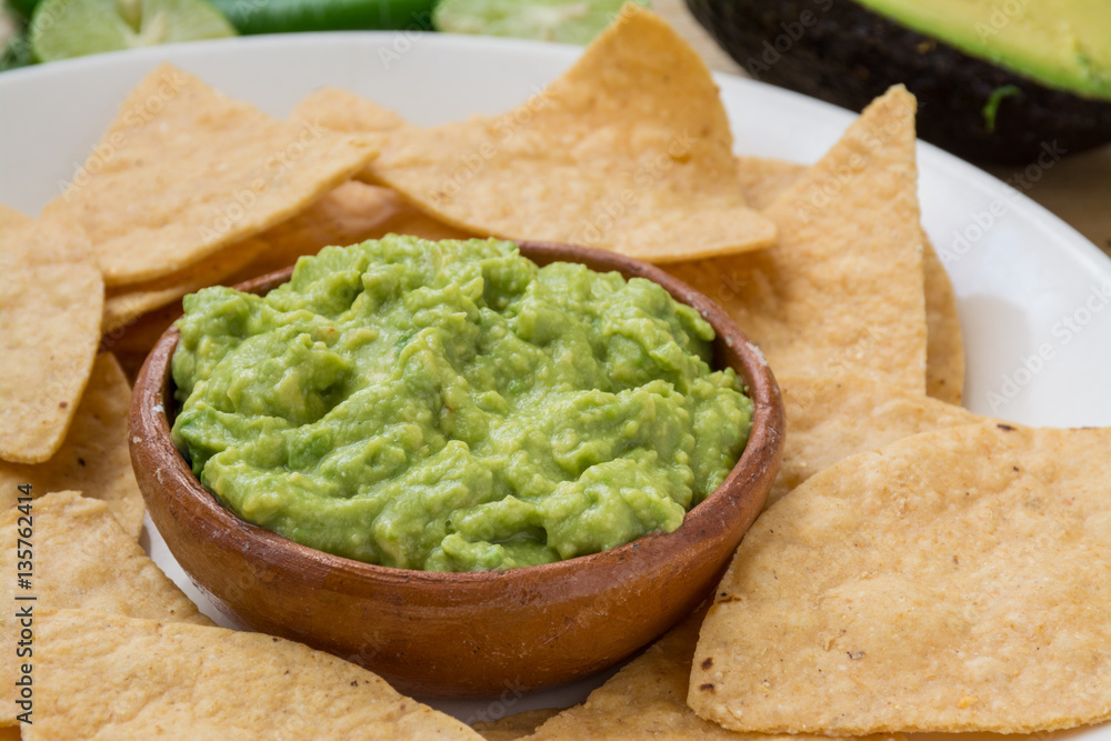 Guacamole dip and tortilla chips on wooden surface Guacamole dip and tortilla chips on wooden surface