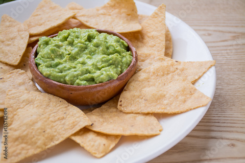 Guacamole dip and tortilla chips on wooden surface