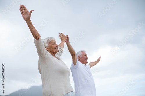 Senior couple standing with arms outstretched on the beach