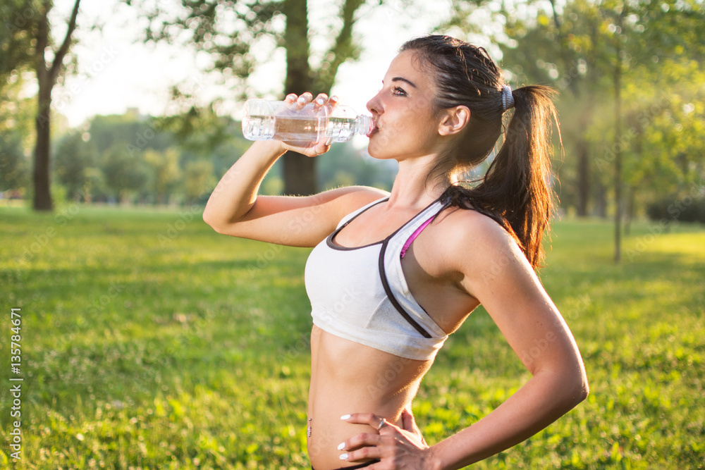Young athletic girl drinking water after running in the park at sunset. Young athletic girl drinking water after running in the park at sunset.