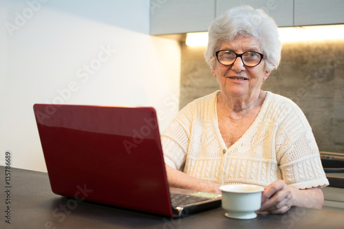 Senior woman using laptop computer while having coffee break at home.