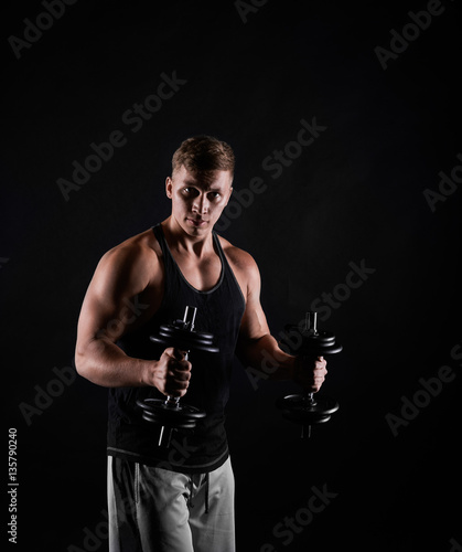 Fitness trainer with dumbbells on black background. Man making training exercises. Concept of healthy life. Strong person look to the camera.