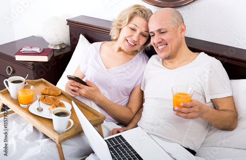 Couple posing with breakfast and laptop in bed photo