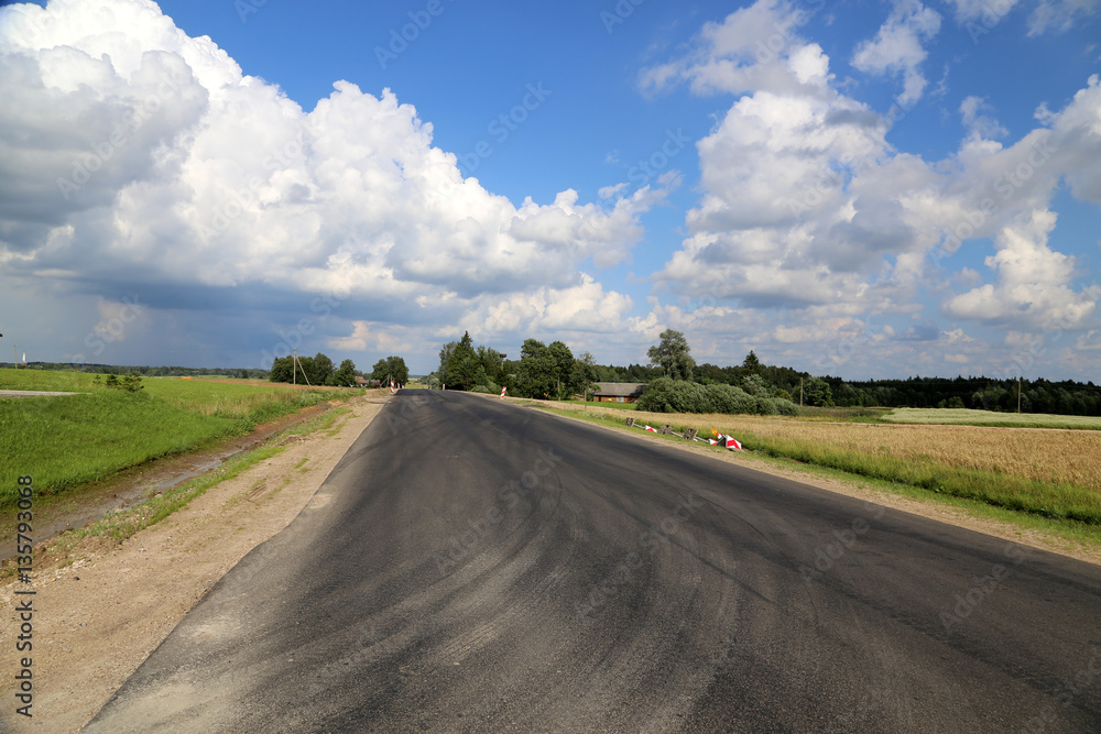Landstraße mit Reifenspuren unter weitem blauem Himmel in Lettland Landstraße mit Reifenspuren unter weitem blauem Himmel in Lettland
