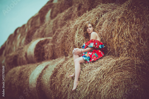 Happy woman on hay stack in sunny day. Beauty romantic girl outdoors against  . Photo of sexy brunette in a field with haystacks