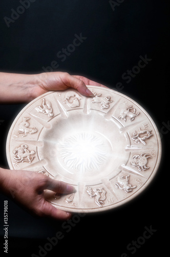 a woman keeping astrology plate with zodiac signs with copy space over a black background 