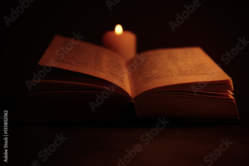 Bible and burning candle on table