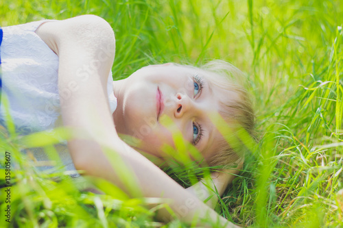 little baby lying in grass outdoors, smiling, looking up at the sun, his hands behind his head, close-up