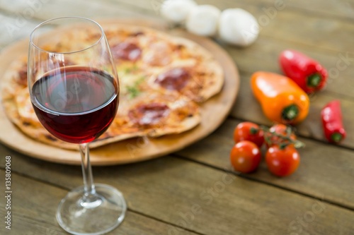 A glass of red wine served with italian pizza in the background