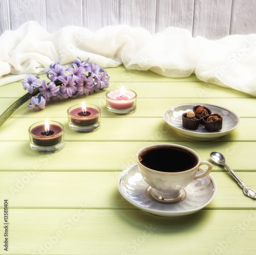 Cup of black coffee, candles and flowers on a wooden background.