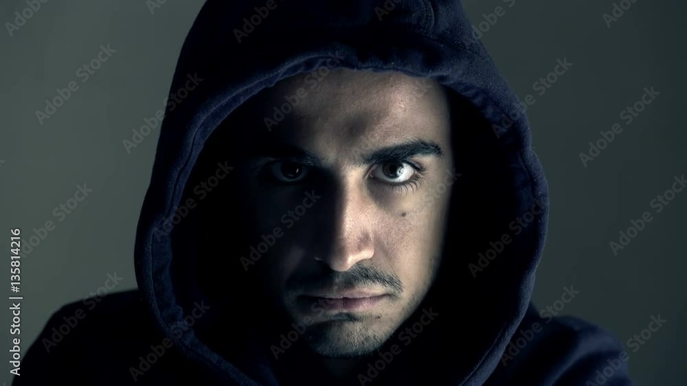 young hooded man looks menacingly at the camera young hooded man looks menacingly at the camera