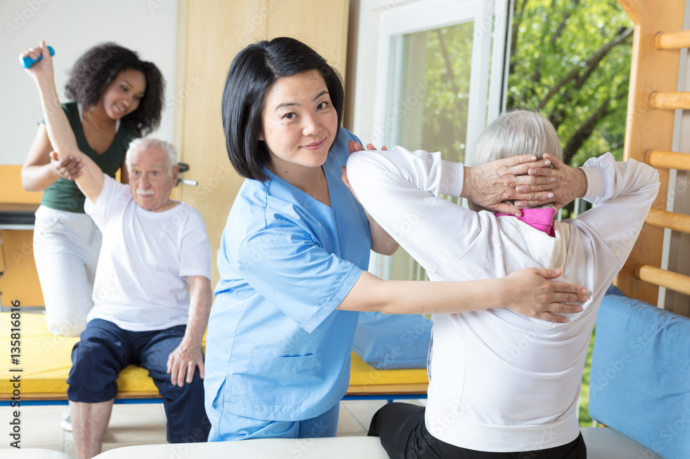 Fototapeta premium Rehab clinic gym. Elderly man and woman assisted by nurses