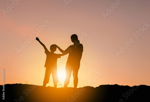 Silhouettes of mother and son playing at sunset evening sky background.