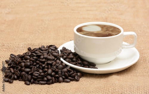 Coffee in cup with roasted beans on jute fabric background