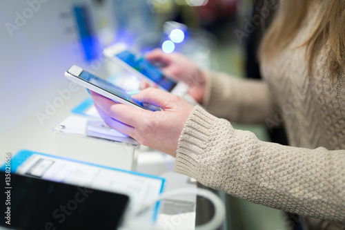Close up shot of beautiful woman shopping. She standing in mobile and tablet shop and choosing next model for her. Selective focus on hand.