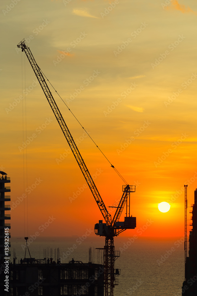 Silhouette of construction tower crane with sunset background at evening time.