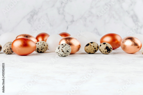 Painted bronze and quail Easter eggs on a marble background.