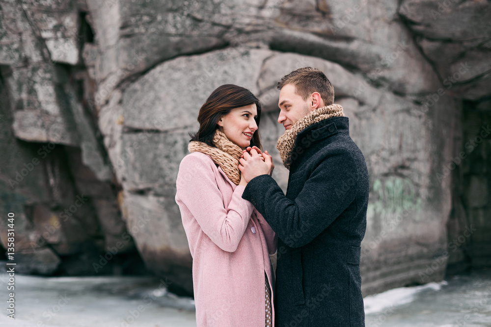 Winter love story. Cute couple in a very beautiful place. They laugh at the frozen lake near high rocks
