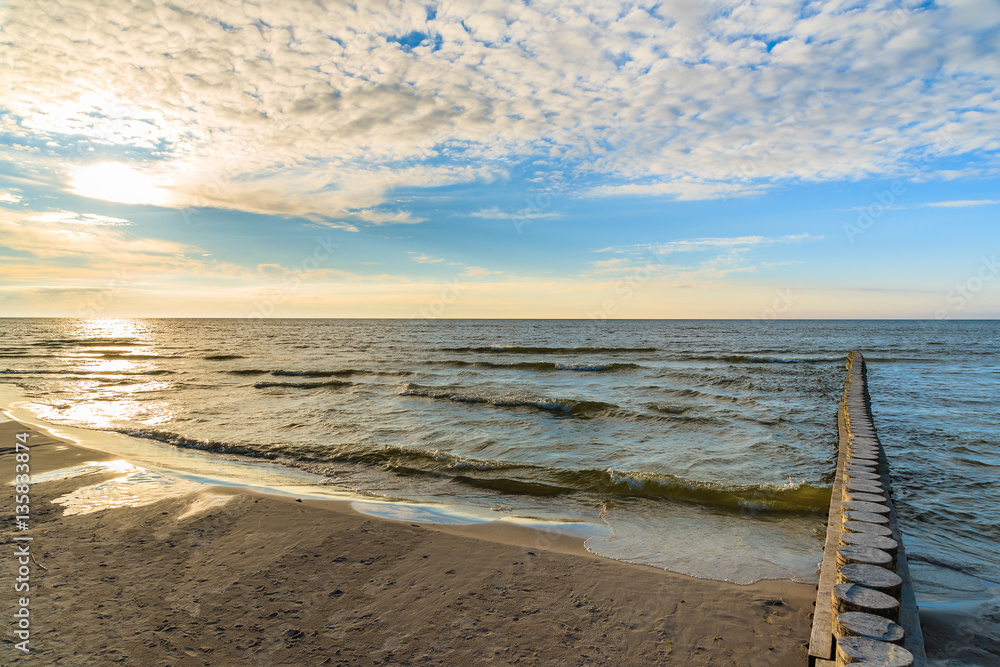 Wooden breakwaters on Leba beach during sunny day with clouds, Baltic Sea, Poland
