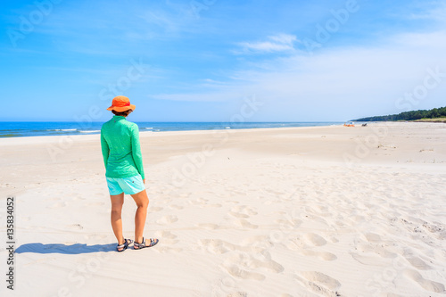 Young woman standing on white sand and looking at beautiful beach, Baltic Sea, Poland