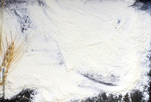 background from the spilled flour and wheat ears on a black baking tray