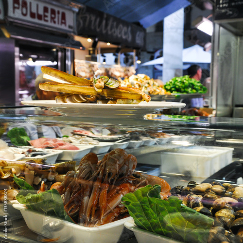 Shrimps, bamboo jack knife clams and mussels on ice in glass case of cafe at Mercat de Sant Josep, Boqueria market Barcelona Spain. Fried Gould's razor shell or Canyut navaja in olive oil and pesto