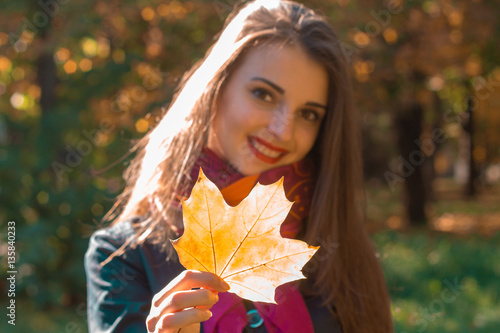 beautiful girl smiling and holding a maple leaf in his hand