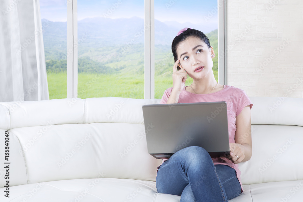 Naklejka premium Pensive woman with laptop in living room