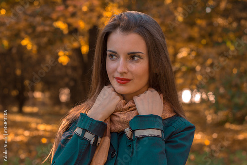 young girl stands in the park looks away and keeps hands for scarf