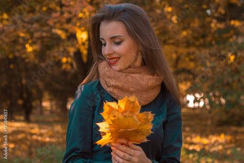 beautiful girl smiling and holding a maple leaf in the hands