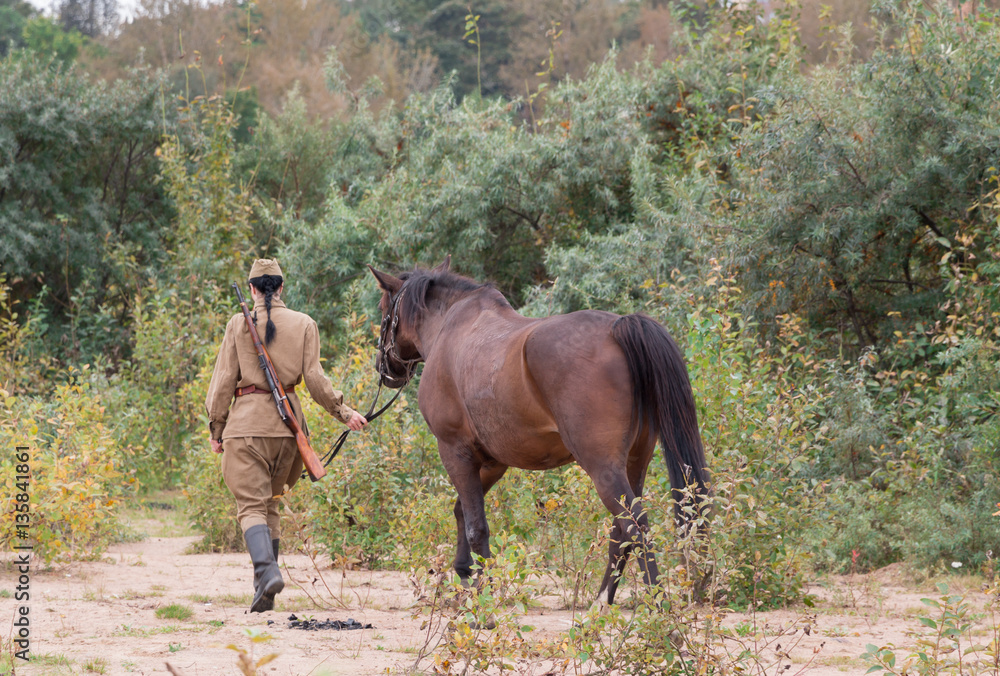 A woman in a uniform walking with a horse in the woods. A woman in a uniform walking with a horse in the woods.
