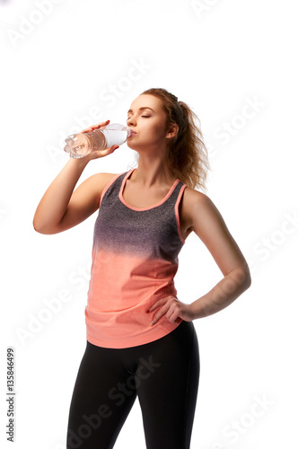 Beautiful athletic girl drinks water after a workout. Woman in sportswear with a bottle of clean water. Attractive young blonde. The woman with pleasure drinking an energy drink.